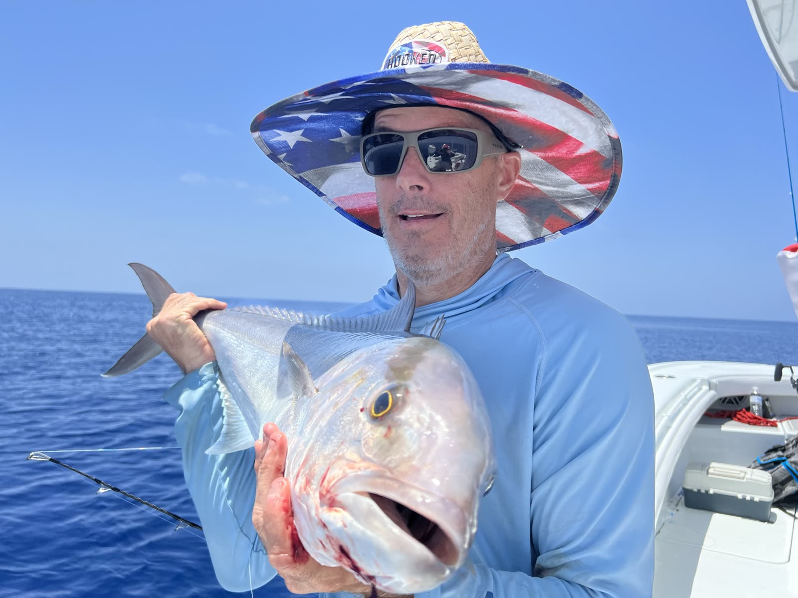 An angler holds a large greater amberjack vertically on a boat offshore
