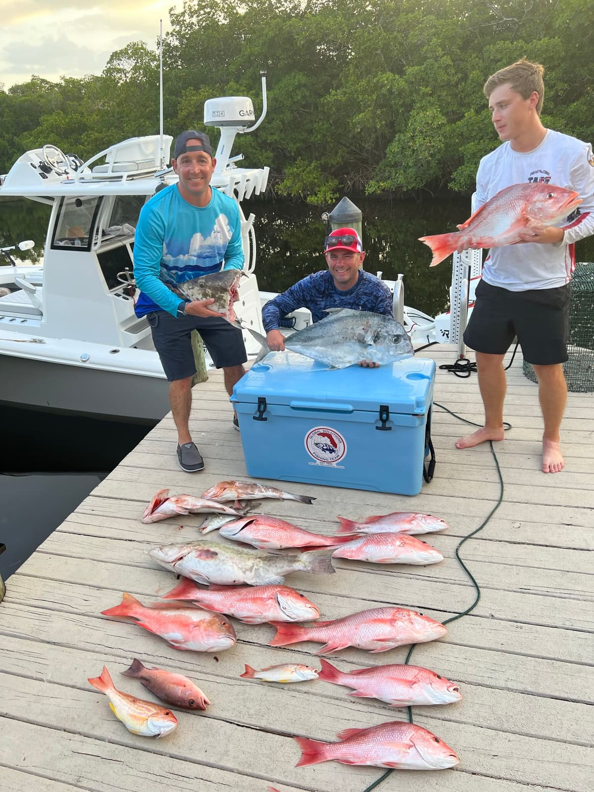 Three anglers displaying a dock catch of red snapper and grouper at golden hour