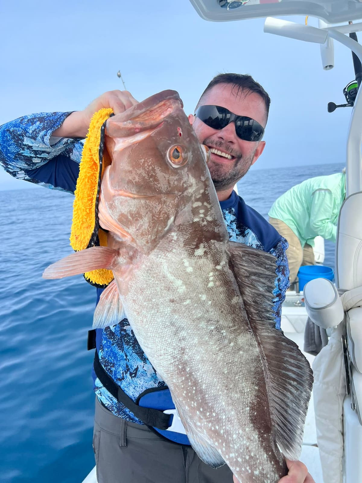 An angler lifts a mottled brown grouper at the boat rail in open Gulf water