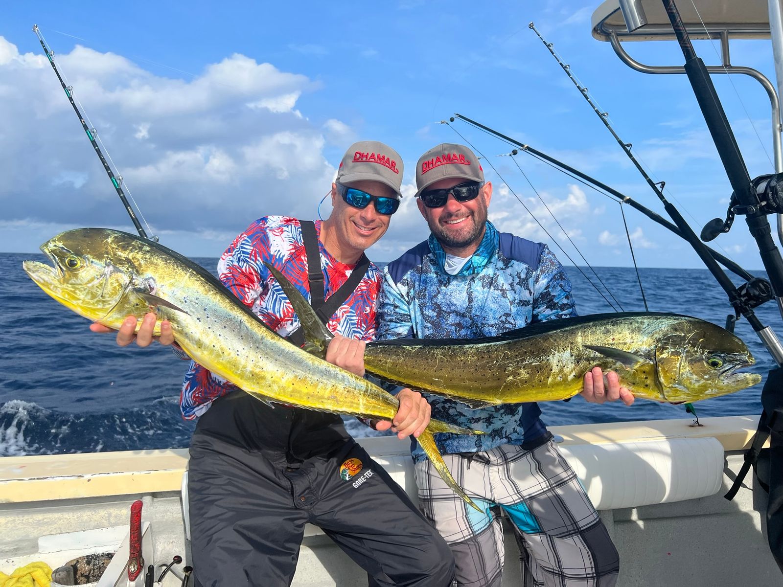 Two smiling men each holding a large yellow mahi mahi fish on an offshore boat.
