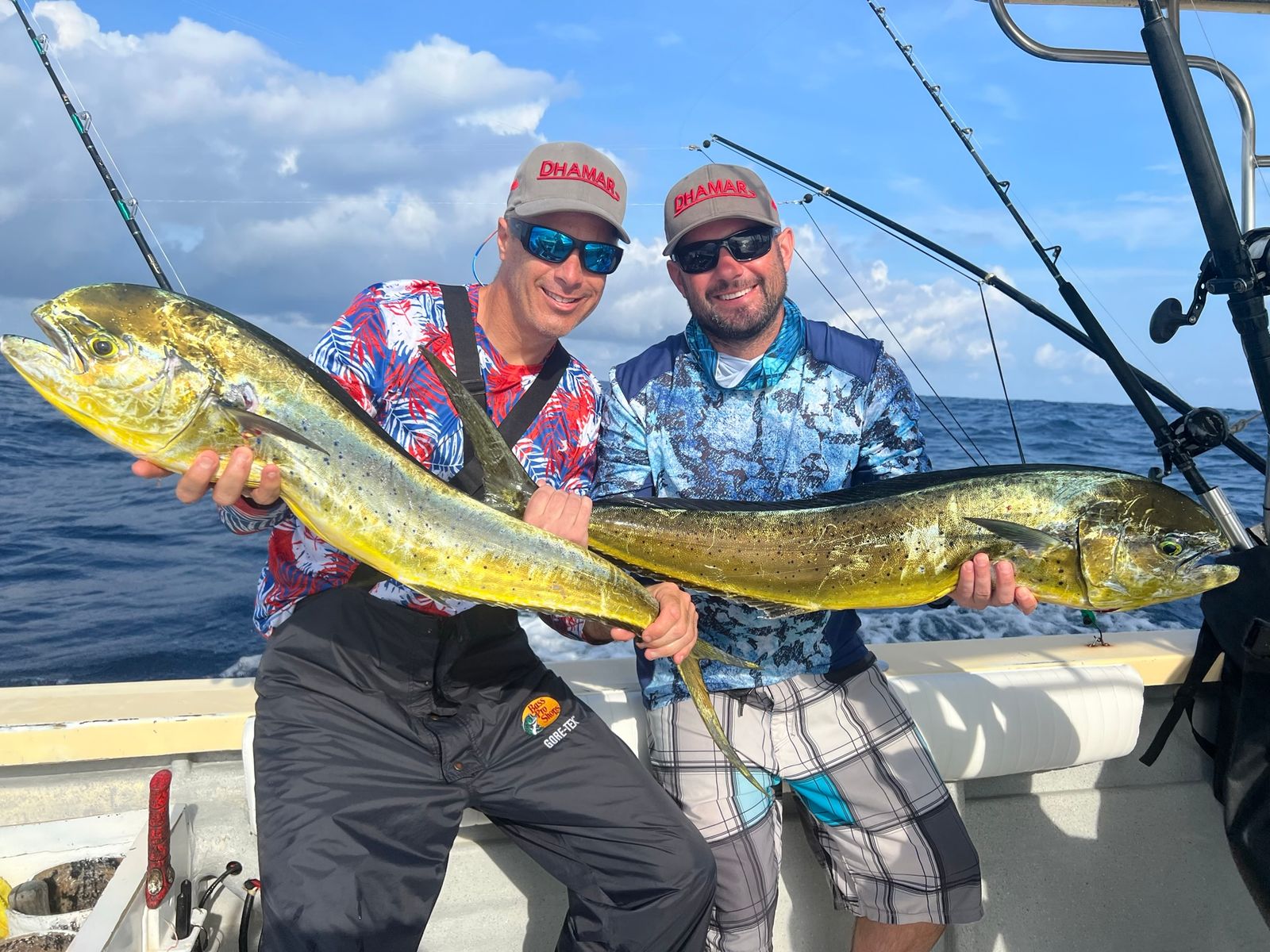 Two smiling men each hold a large mahi mahi fish on an offshore fishing boat.