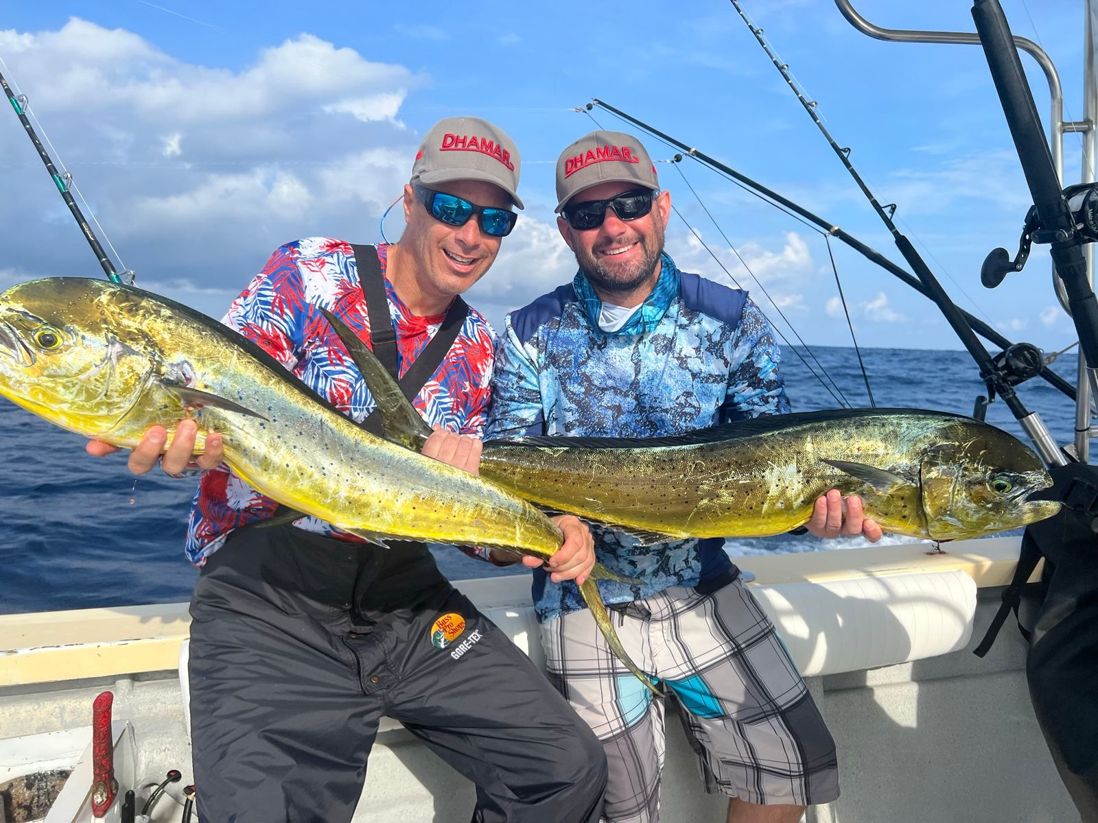 Two smiling men each hold a large mahi mahi fish on an offshore fishing boat.