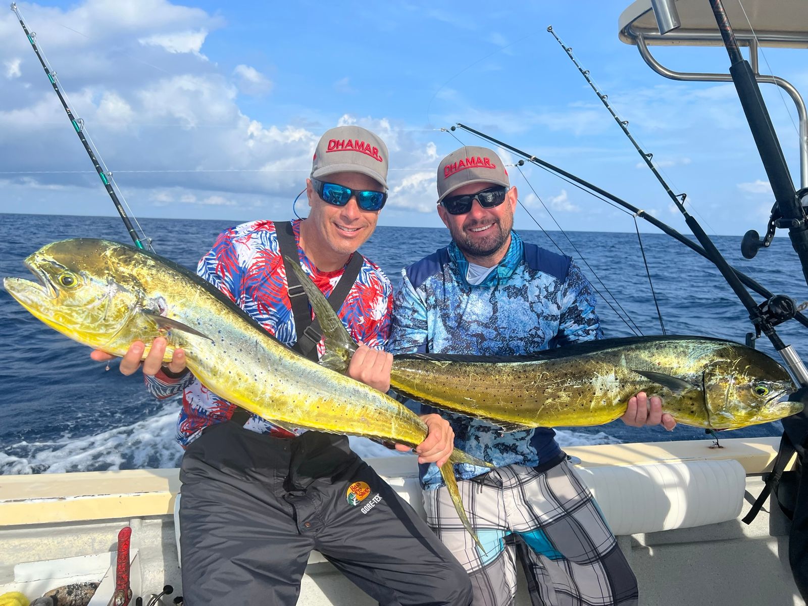 Two smiling men each hold a large mahi mahi fish on an offshore fishing boat, sharpest of this series.