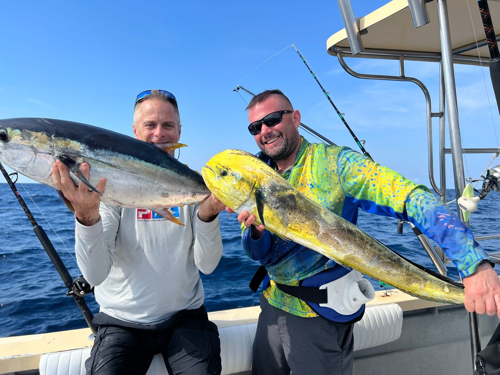 Two smiling men on a boat hold up a tuna and a mahi mahi with a t-top and rods behind them.