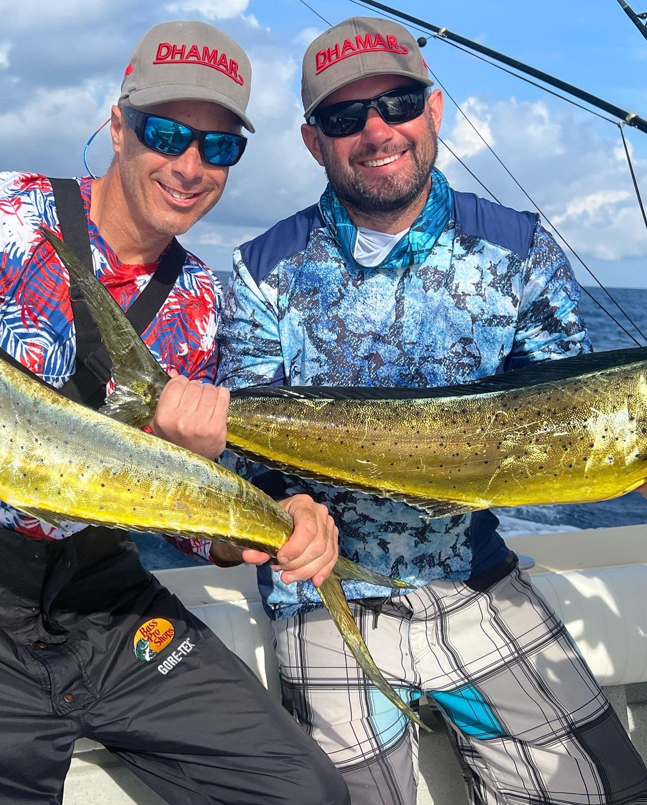 Two smiling men on a boat hold up a large yellow and green mahi mahi fish.
