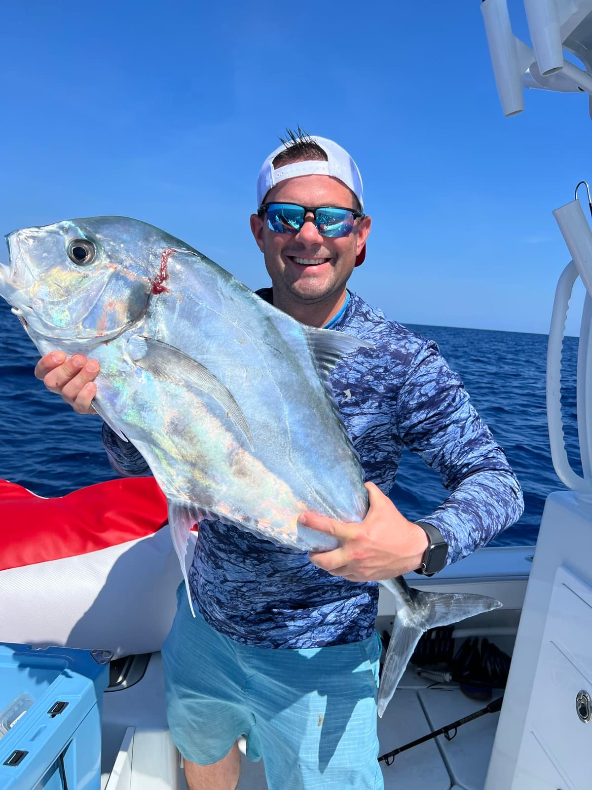 An angler holds a large deep-bodied silver jack on a boat offshore