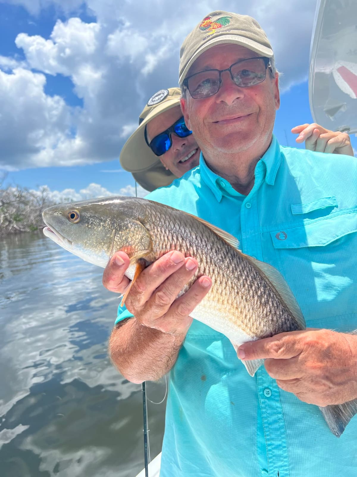 An angler holds a coppery-bronze redfish in a mangrove backwater