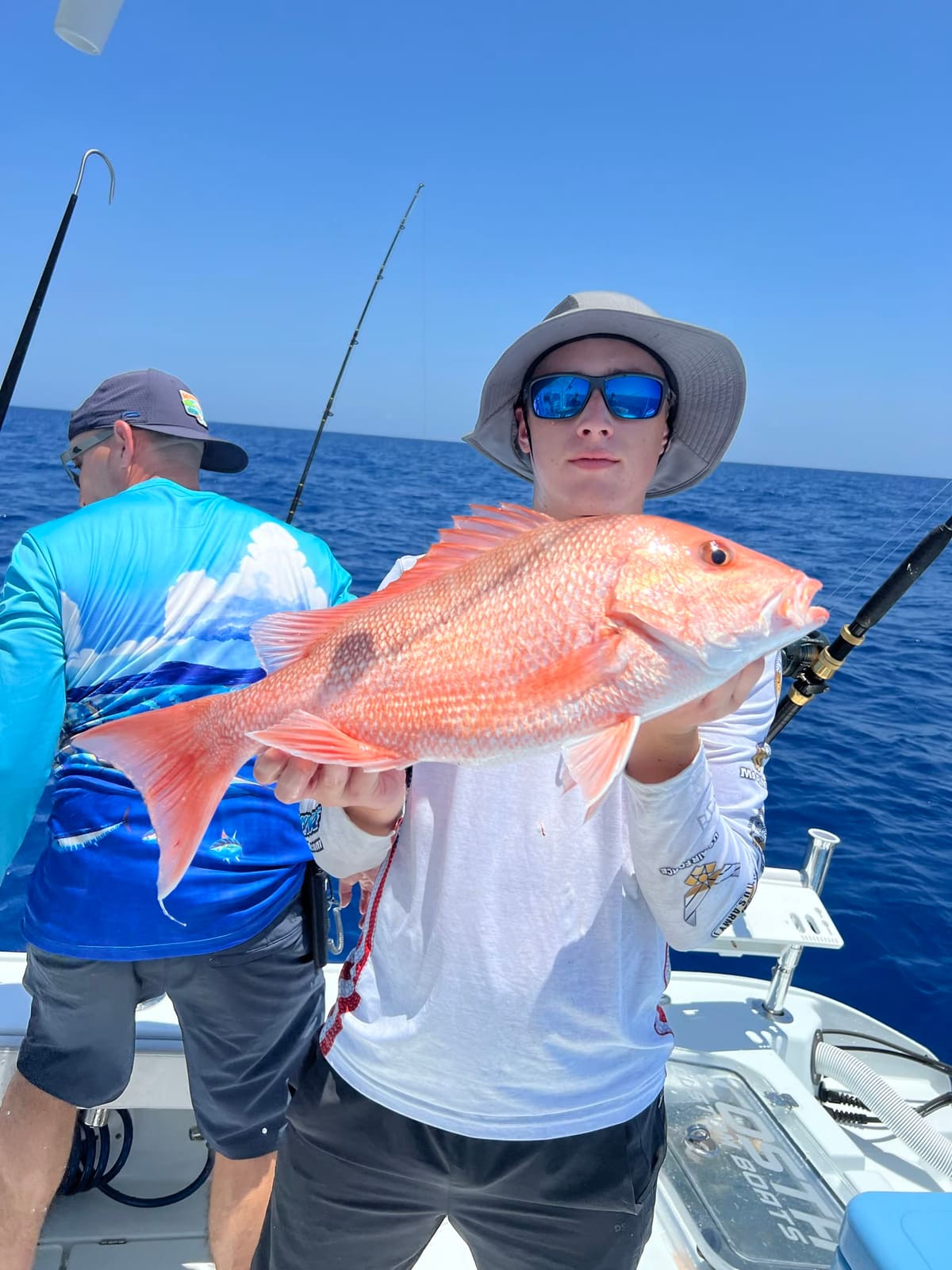 An angler holds a bright red snapper chest-high on a boat in open Gulf water