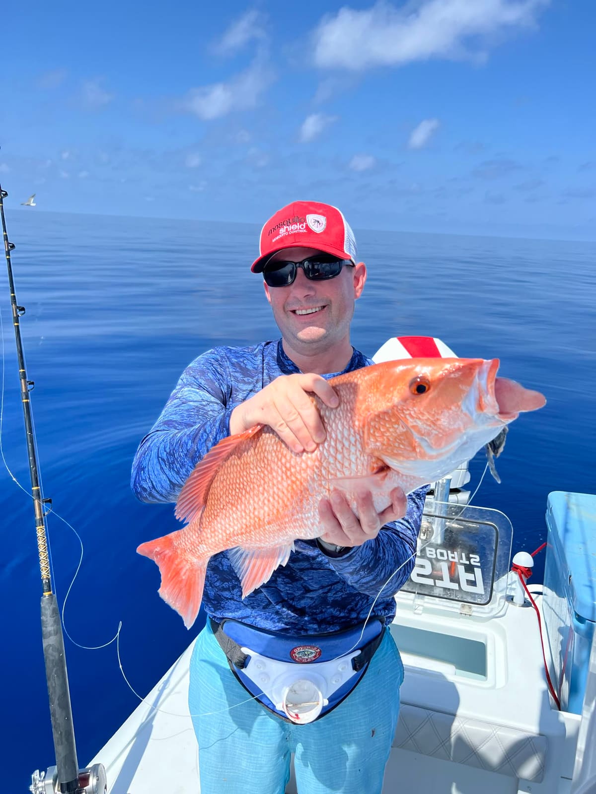 An angler holds a bright red snapper close to the camera on a boat offshore